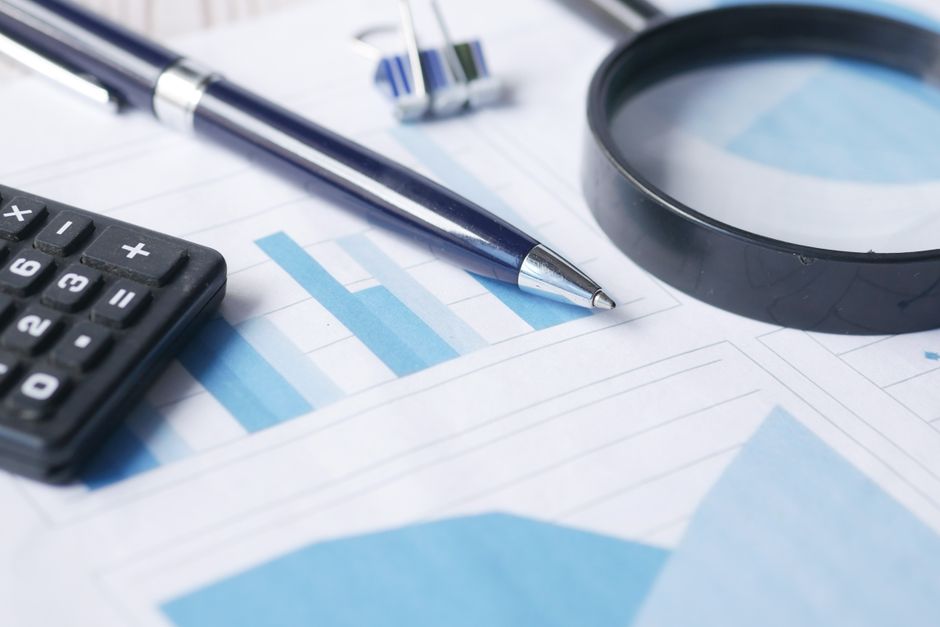pen, calculator and magnifying glass sitting on top of reports